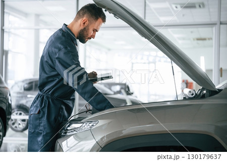 View from the side. Car repairman is in the garage with automobile 130179637