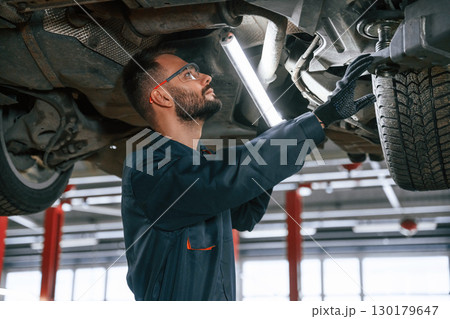 Under the vehicle, fixing. Car repairman is in the garage with automobile 130179647