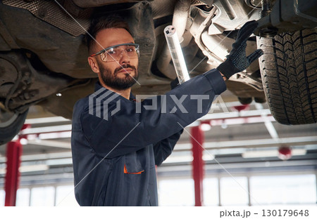 Under the vehicle, fixing. Car repairman is in the garage with automobile 130179648