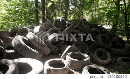 Discarded rubber tires are piled high in a forested area, showcasing the problem of pollution and its impact on local ecology. The sight emphasizes the urgent need for environmental action. Discarded rubber tires are piled high in a forested area, showcasing the problem of pollution and its impact on local ecology. The sight emphasizes the urgent need for environmental action. 130180220