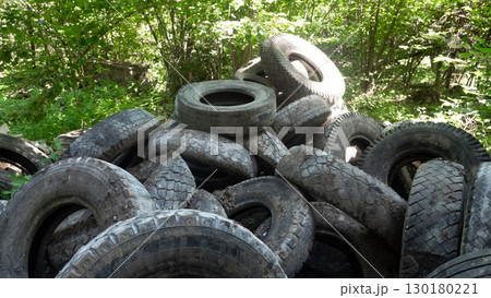 A large collection of discarded rubber tires sits abandoned in a wooded area, highlighting significant ecological problems and the dangers of pollution. 130180221