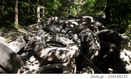 A large accumulation of discarded rubber tires piles up in a forest environment, exposing the critical ecological issues related to pollution and waste management. A large accumulation of discarded rubber tires piles up in a forest environment, exposing the critical ecological issues related to pollution and waste management. 130180235