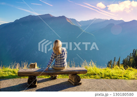 Mountain landscape on a sunny day. A woman sits on the bench and looks at the mountains. Grossglockner High Alpine Road. Austria, Europe 130180580