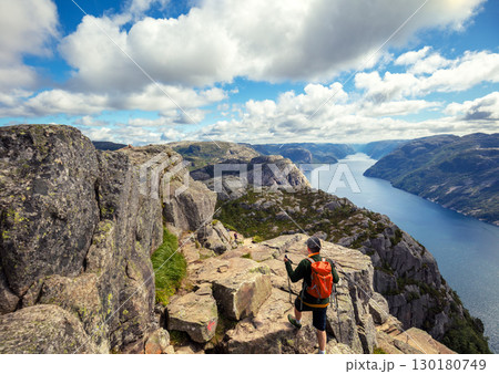 Man climbing to the top of a cliff. View of the beautiful Lysefjord on a cloudy day. Rocky shore of the majestic Lysefjord. Beautiful wild nature of Norway 130180749