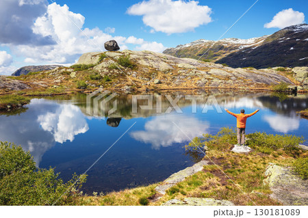 Man with hands in the air standing on a lakeshore in the mountains. Nature park in Sauda municipality, Rogaland fylke. Beautiful nature of Norway, Europe Man with hands in the air standing on a lakeshore in the mountains. Nature park in Sauda municipality, Rogaland fylke. Beautiful nature of Norway, Europe 130181089