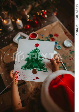 Small child indoors at home at Christmas, painting pictures with christmas tree. 130181349