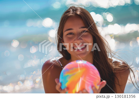 Cheerful woman embracing a sunny beach day with a colorful beach ball 130181356