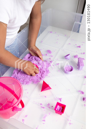 Child playing with purple kinetic sand engaging in creative playtime fun 130181490