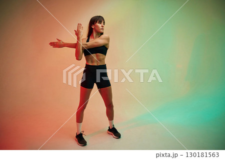 Standing and doing exercises. Young woman in fitness clothes is in the studio 130181563