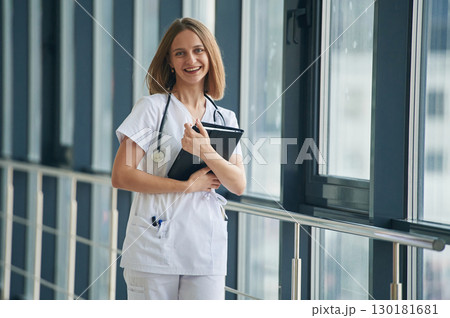 Document in hands. Female doctor in white coat is in the hall 130181681