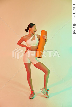 Happy person holding yoga mat. Young fitness woman in sportive clothes against background in studio 130182011