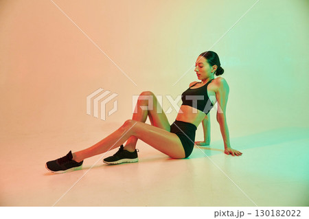 In black sportive clothes. Young fitness woman is against background in studio 130182022