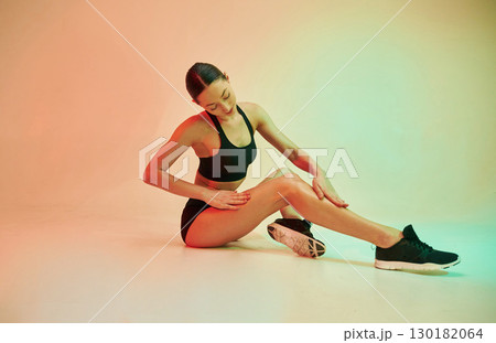 Touching clean legs after depilation. Young fitness woman in sportive clothes against background in studio Touching clean legs after depilation. Young fitness woman in sportive clothes against background in studio 130182064