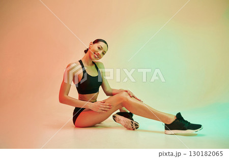 Touching clean legs after depilation. Young fitness woman in sportive clothes against background in studio Touching clean legs after depilation. Young fitness woman in sportive clothes against background in studio 130182065