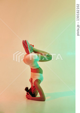 Doing head stand. Young fitness woman in sportive clothes against background in studio Doing head stand. Young fitness woman in sportive clothes against background in studio 130182102