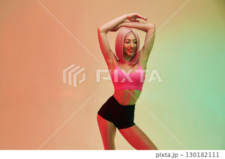 With hands up. Sportive woman with pink wig is against background 130182111