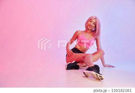 Taking a rest on the floor. Sportive woman with pink wig is against background 130182161