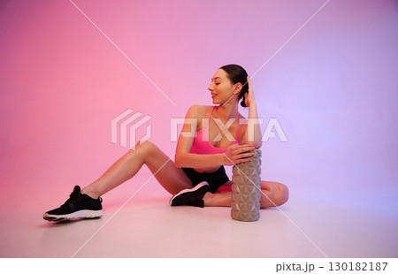 Wellbeing, with roller. Young fitness woman in sportive clothes against background in studio 130182187