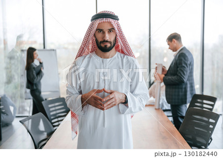 People behind Muslim businessman that is in traditional outfit with colleagues in office People behind Muslim businessman that is in traditional outfit with colleagues in office 130182440