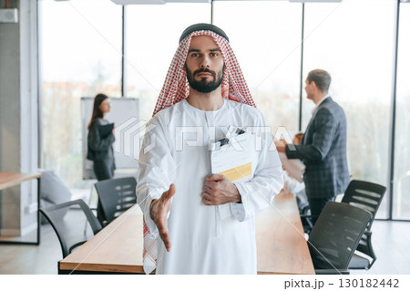 People behind Muslim businessman that is in traditional outfit with colleagues in office 130182442