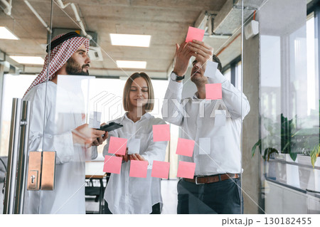 Using stickers on the glass. Muslim businessman in traditional outfit with colleagues in office Using stickers on the glass. Muslim businessman in traditional outfit with colleagues in office 130182455