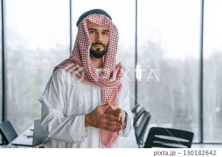 Against panoramic windows. Successful Muslim businessman in traditional outfit in his office Against panoramic windows. Successful Muslim businessman in traditional outfit in his office 130182642