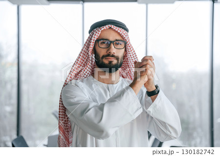 Young investor is standing. Successful Muslim businessman in traditional outfit in his office Young investor is standing. Successful Muslim businessman in traditional outfit in his office 130182742