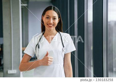 Standing and posing. Female doctor in white coat is indoors Standing and posing. Female doctor in white coat is indoors 130183258