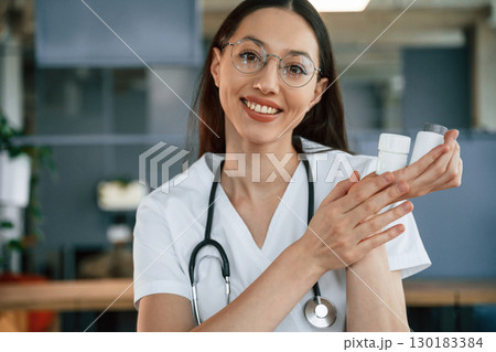 In glasses. Sitting by the table. Female doctor in white coat is indoors 130183384