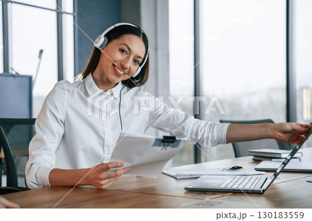 Technical support. In headphones. Businesswoman is indoors in the office 130183559