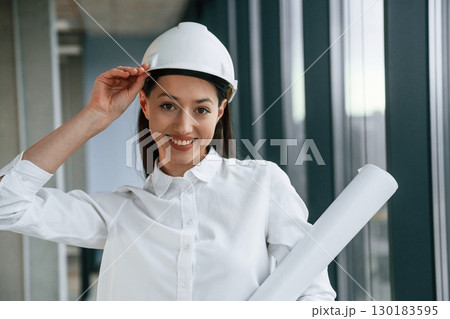 Female architect in hard hat and in white clothes is indoors Female architect in hard hat and in white clothes is indoors 130183595