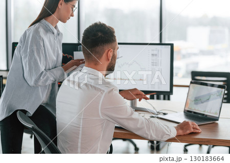 Brokers with monitors with graphs on the table. Two employees are working in the office together Brokers with monitors with graphs on the table. Two employees are working in the office together 130183664