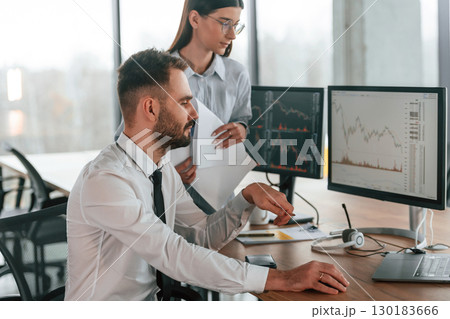 Brokers with monitors with graphs on the table. Two employees are working in the office together Brokers with monitors with graphs on the table. Two employees are working in the office together 130183666
