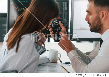 Brokers with monitors with graphs on the table. Two employees are working in the office together 130183671