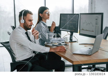 By the table with laptop. Two employees are working in the office together By the table with laptop. Two employees are working in the office together 130183814