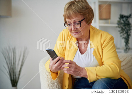 Holding smartphone. Senior elderly woman is at home in the living room Holding smartphone. Senior elderly woman is at home in the living room 130183998