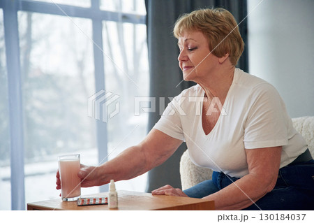 Drink with anti flu medicament. Senior elderly woman is at home in the living room 130184037