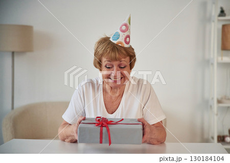 What's in the gift box. Celebrating birthday. Senior elderly woman is at home in the living room 130184104