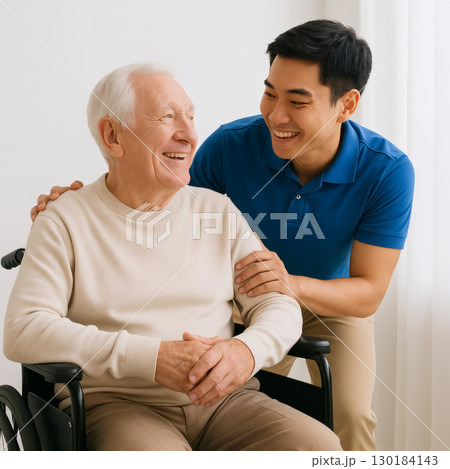 明るい室内で介助するアジア人介護士と笑顔の高齢男性 130184143