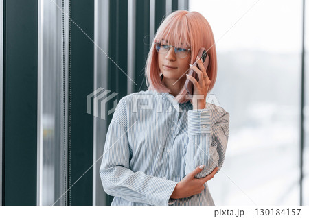Talking by phone. Woman with pink hair is in the office. Young worker 130184157