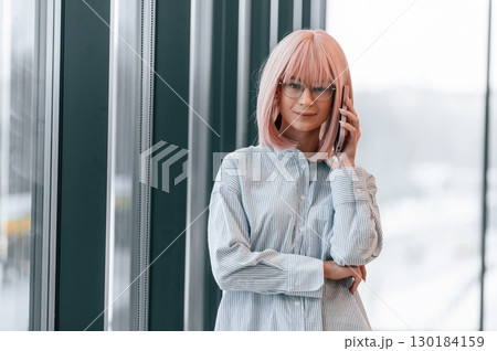 Talking by phone. Woman with pink hair is in the office. Young worker 130184159