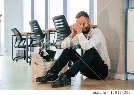 Depressed, sitting on the floor. Unemployed man is with personal belongings after being fired Depressed, sitting on the floor. Unemployed man is with personal belongings after being fired 130184295