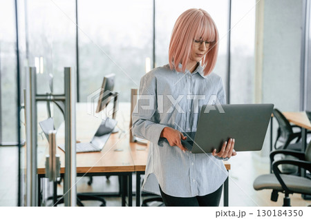 Silver colored laptop in hands. Woman with pink hair is in the office. Young worker 130184350