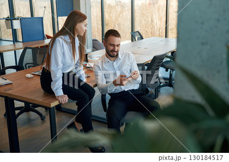 Showing information in the phone. Man and woman employees are working in the office Showing information in the phone. Man and woman employees are working in the office 130184517