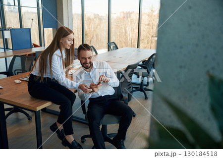 Showing information in the phone. Man and woman employees are working in the office Showing information in the phone. Man and woman employees are working in the office 130184518