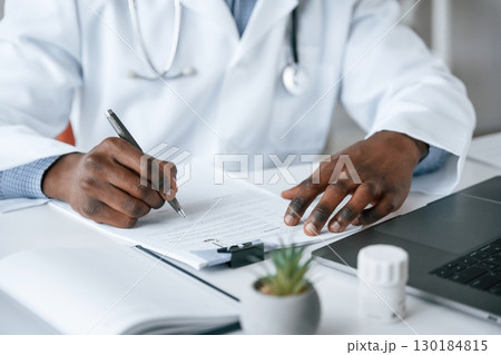 Filling in the document, writing by using pen. Black man as doctor in the clinic office Filling in the document, writing by using pen. Black man as doctor in the clinic office 130184815