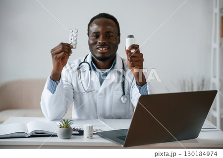 Holding pills in hands. Black man as doctor in the clinic office Holding pills in hands. Black man as doctor in the clinic office 130184974