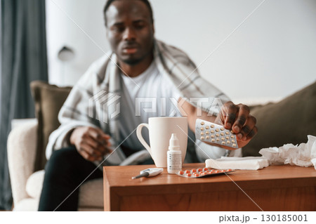 Holding pills that are on the table. Sick black man is at home Holding pills that are on the table. Sick black man is at home 130185001