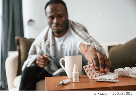 Holding pills that are on the table. Sick black man is at home 130185003