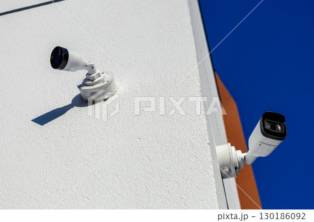 Two security cameras are installed on the corner of a contemporary building, monitoring the surroundings under a clear blue sky Two security cameras are installed on the corner of a contemporary building, monitoring the surroundings under a clear blue sky 130186092